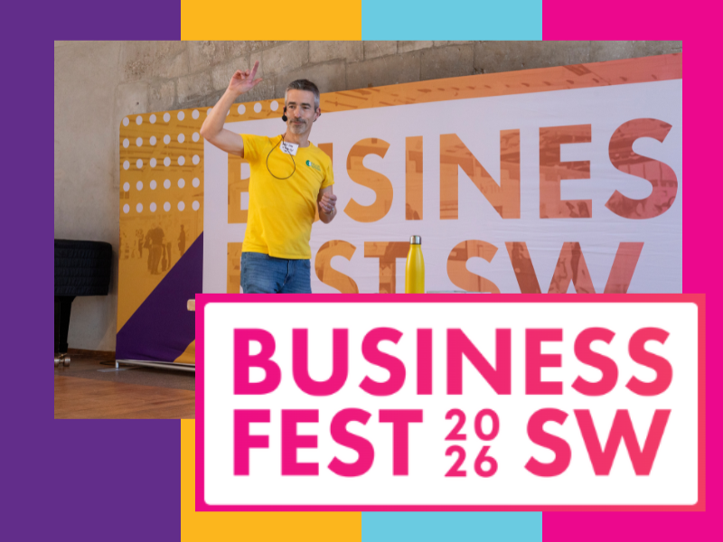 LinkedIn speaker based in Devon Ashley Leeds, the 15-minute guy, delivering a keynote at Business Fest South West 2026, standing on stage in a yellow shirt in front of a large colourful event banner